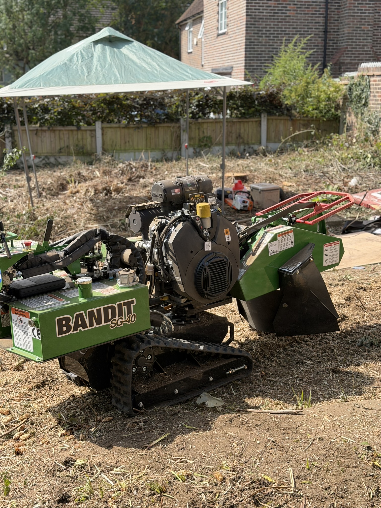 A green Bandit SG-40 tracked stump grinder on a cleared plot in Romford, with cut vegetation and cleared ground behind