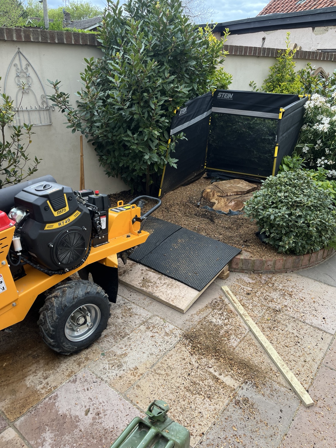 The hybrid pedestrian stump grinder positioned on ground protection boards, with a debris guard set up around the stump and mats protecting the paving