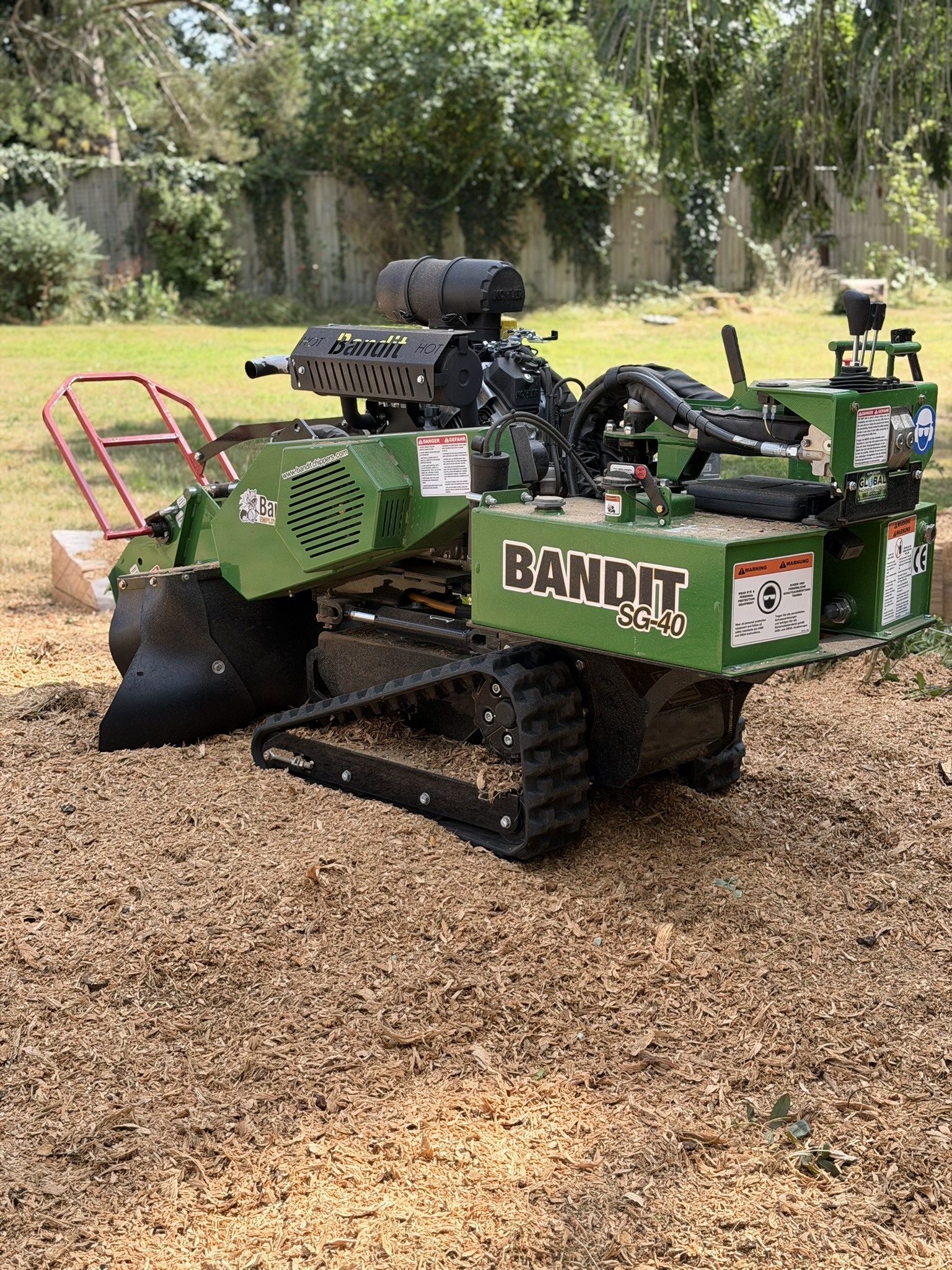 The cleared area after grinding, now a bed of fresh wood chippings where the cedar stump used to be, with the Bandit SG-40 grinder parked on it